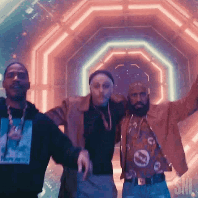 three men are dancing in front of a sign that says ' snl ' on it