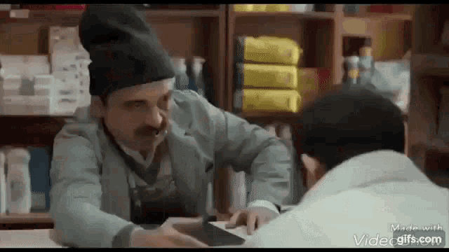a man is sitting at a table in a store talking to another man .