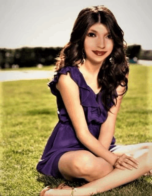 a woman in a purple dress is sitting in the grass with her legs crossed .