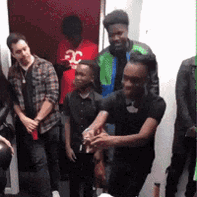 a group of people are standing in a room with a man wearing a red shirt with the letter c on it .