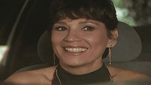 a woman wearing earrings and a black top is smiling