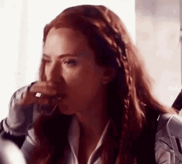 black widow is drinking a glass of wine from a glass while sitting at a table .
