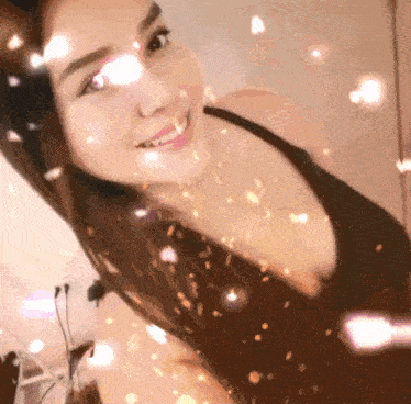 a woman in a black top is smiling with sparkles coming out of her hair