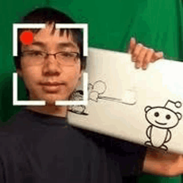 a young man wearing glasses is holding a laptop with a reddit logo on it .