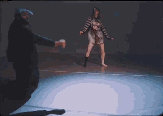 a woman in a striped dress is dancing in front of a man