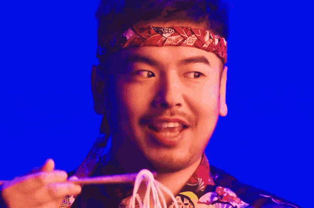 a man wearing a headband is eating noodles from chopsticks