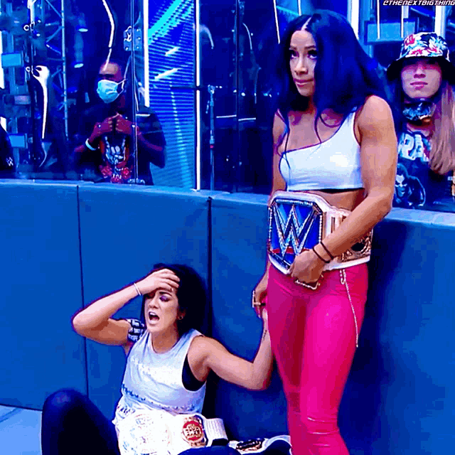 a female wrestler is standing next to a female wrestler who is sitting down