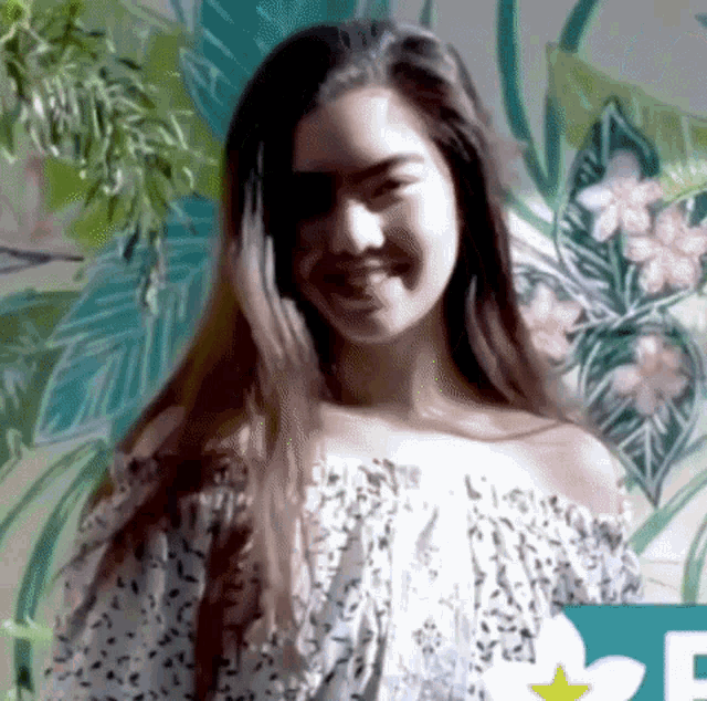 a young woman with long hair is smiling in front of a wall with flowers on it .