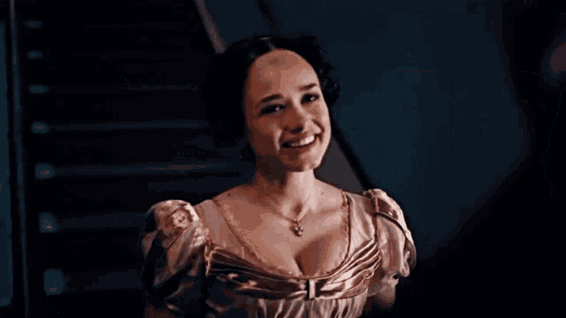 a woman in a dress and necklace is smiling in front of a staircase .
