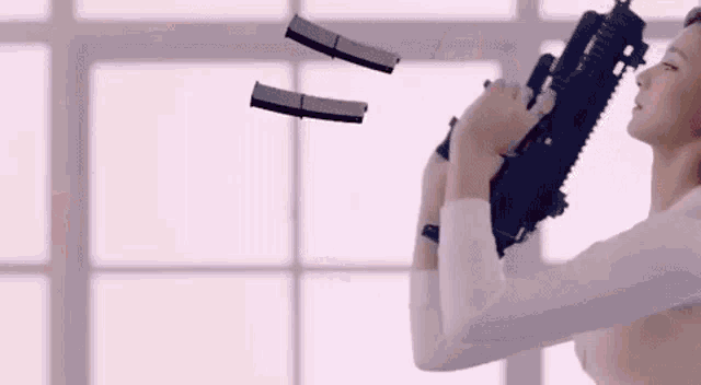 a woman is holding a gun in front of a window while bullets are falling from the ceiling .