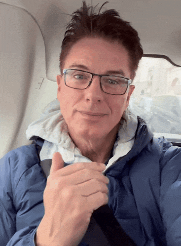 a man wearing glasses and a blue jacket is smiling