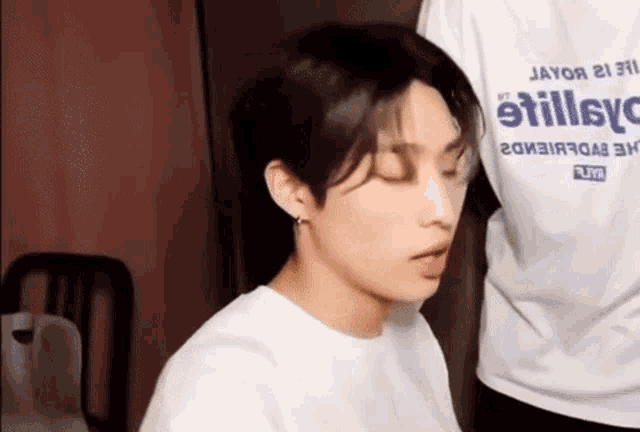 a young man wearing a white t-shirt and earrings is sitting in a room with his eyes closed .
