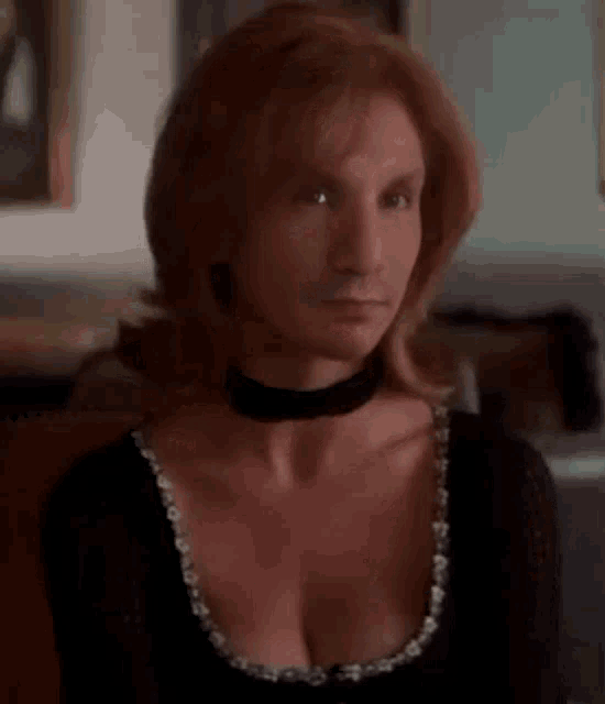 a woman with red hair is wearing a choker around her neck and a black top .