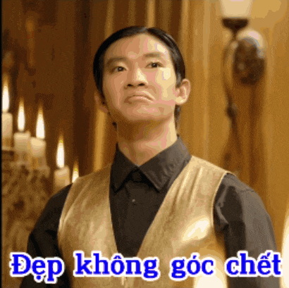 a man wearing a black shirt and a gold vest is standing in front of candles and says dep không goc chet