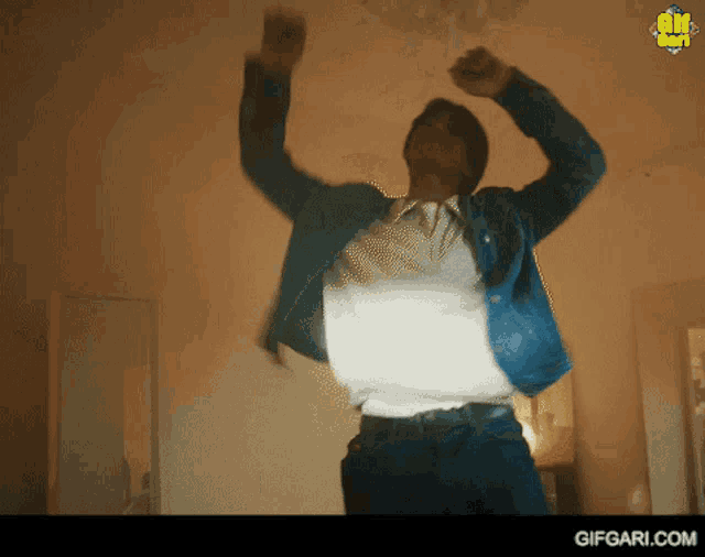 a man in a blue jacket is dancing in a room with gifgari.com on the bottom right