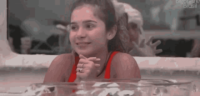 a woman in a red tank top is sitting in a pool of water and smiling .
