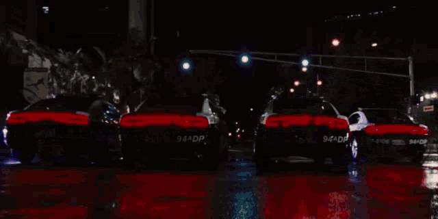 a row of police cars are parked on a wet street at night