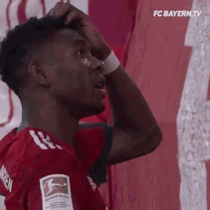 a soccer player scratches his head in front of a red and white banner that says fc bayern.tv