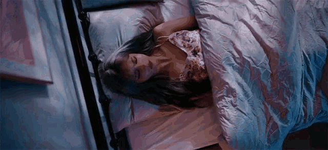 a woman is sleeping in a bed with a purple blanket and pillows .