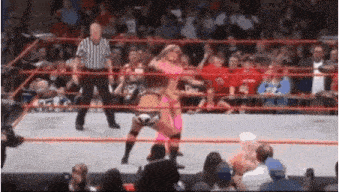 two women are wrestling in a wrestling ring while a referee looks on .