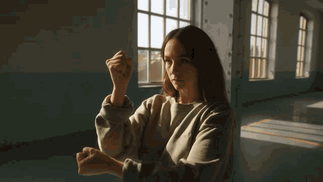 a woman in a grey sweatshirt holds her fist up