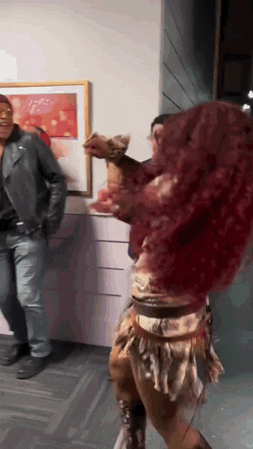 a woman with red hair is dancing in a room with a man in a leather jacket standing behind her .