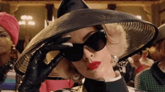 a woman wearing a hat , sunglasses and gloves is covering her eyes .