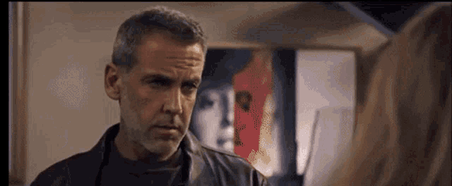 a man in a black leather jacket is looking at a woman in front of a painting .