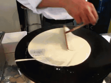 a person is making a pancake on a black plate