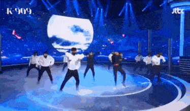 a group of people are dancing on a stage with a sign that says k-909
