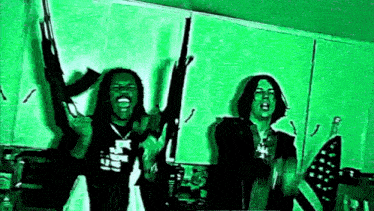 two men are standing next to each other holding guns in a kitchen .