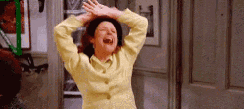 a woman in a yellow jacket and black hat is laughing with her arms in the air .