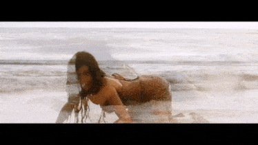 a woman in a bikini is kneeling on the beach looking at the ocean .