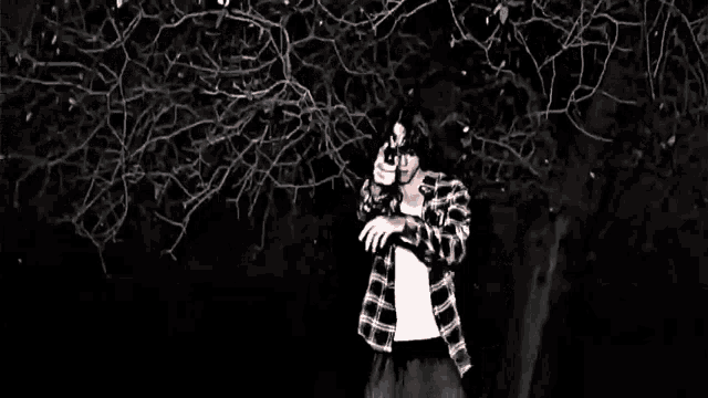 a black and white photo of a man in a plaid shirt standing in the woods .