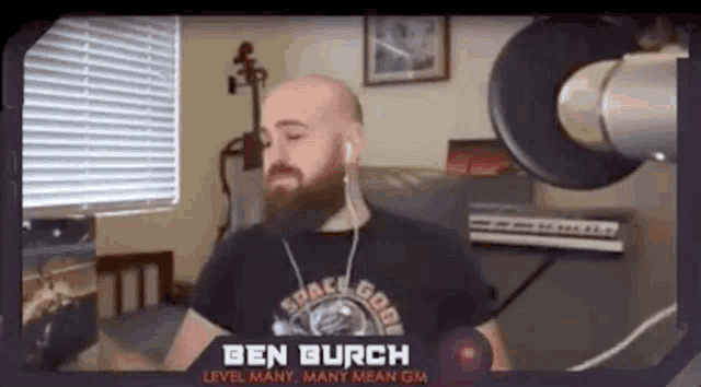 a bald man with a beard is standing in front of a microphone in a living room .
