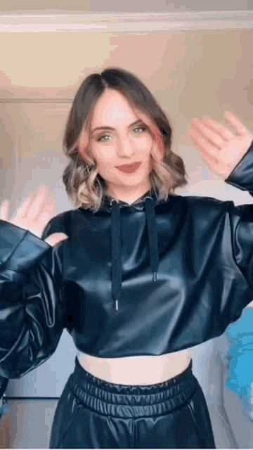 a woman wearing a black crop top and leather pants is dancing in a room .