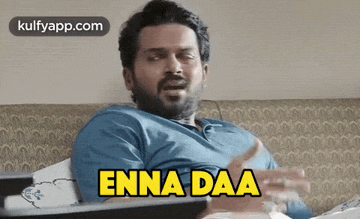 a man with a beard is sitting on a couch and says enna daa .