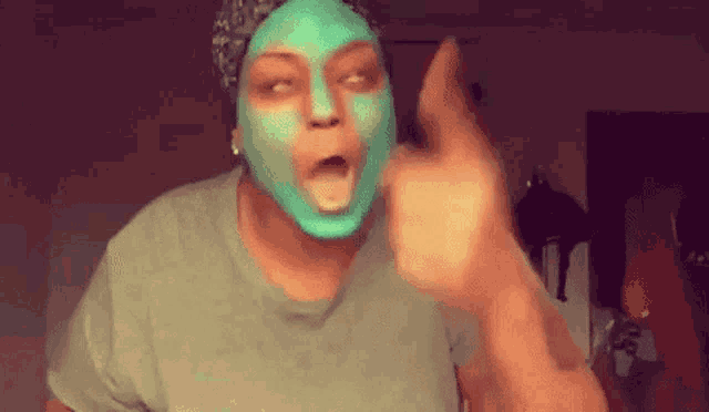 a woman with a green mask on her face is pointing her finger at the camera .