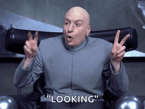 a bald man is sitting in a chair and making a peace sign with the words " looking " behind him