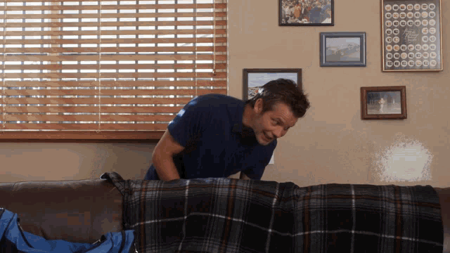 a man standing on a couch with a plaid blanket on it
