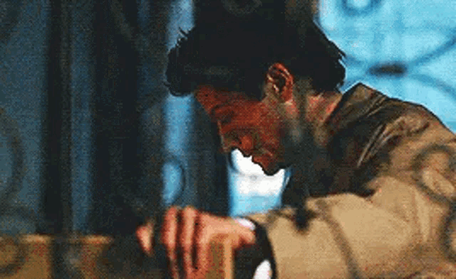 a man in a trench coat is sitting at a table holding a bottle of wine .