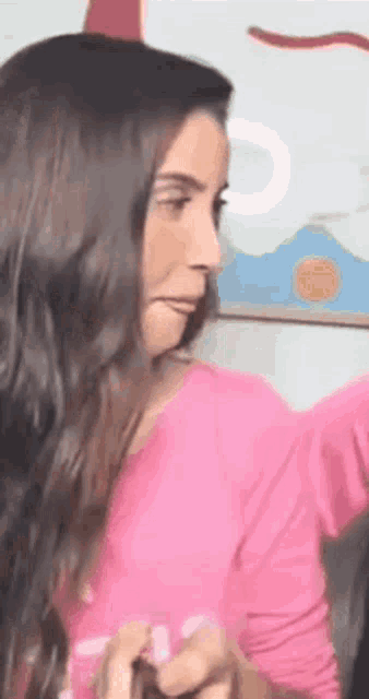 a woman with long hair is wearing a pink shirt and making a face .