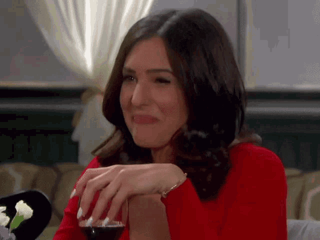 a woman in a red sweater is smiling while holding a glass of wine