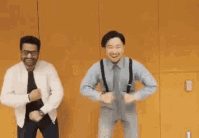 two men are standing next to each other and dancing in front of a yellow wall .