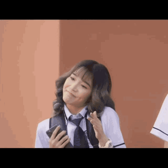 a girl in a school uniform is holding a cell phone in her hand .