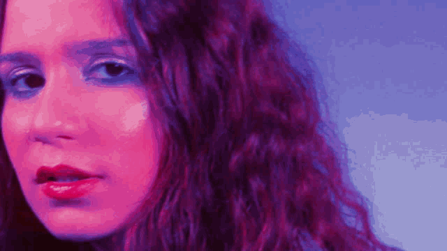 a close up of a woman 's face with purple and pink lighting behind her .