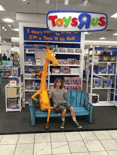 a boy sits on a bench in front of a toys r us store
