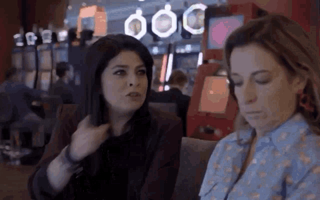 two women are sitting next to each other in front of a slot machine .