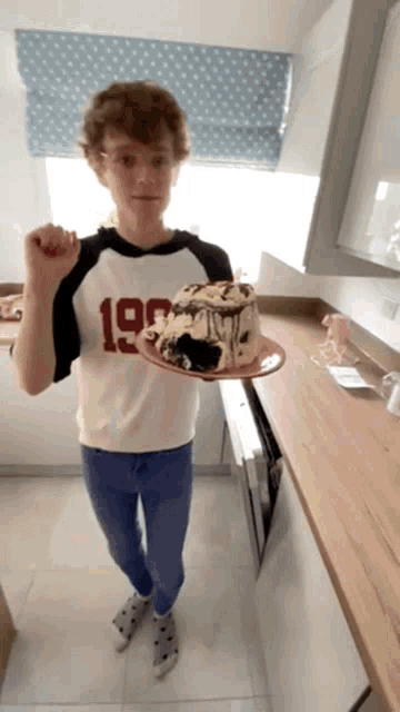 a boy wearing a shirt with the number 19 on it holds a cake on a plate