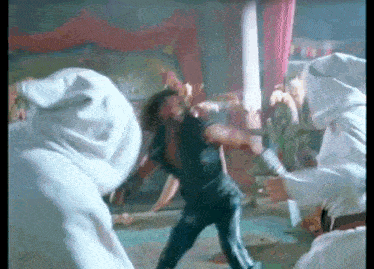 a man in a black shirt is fighting a group of people in white hats .
